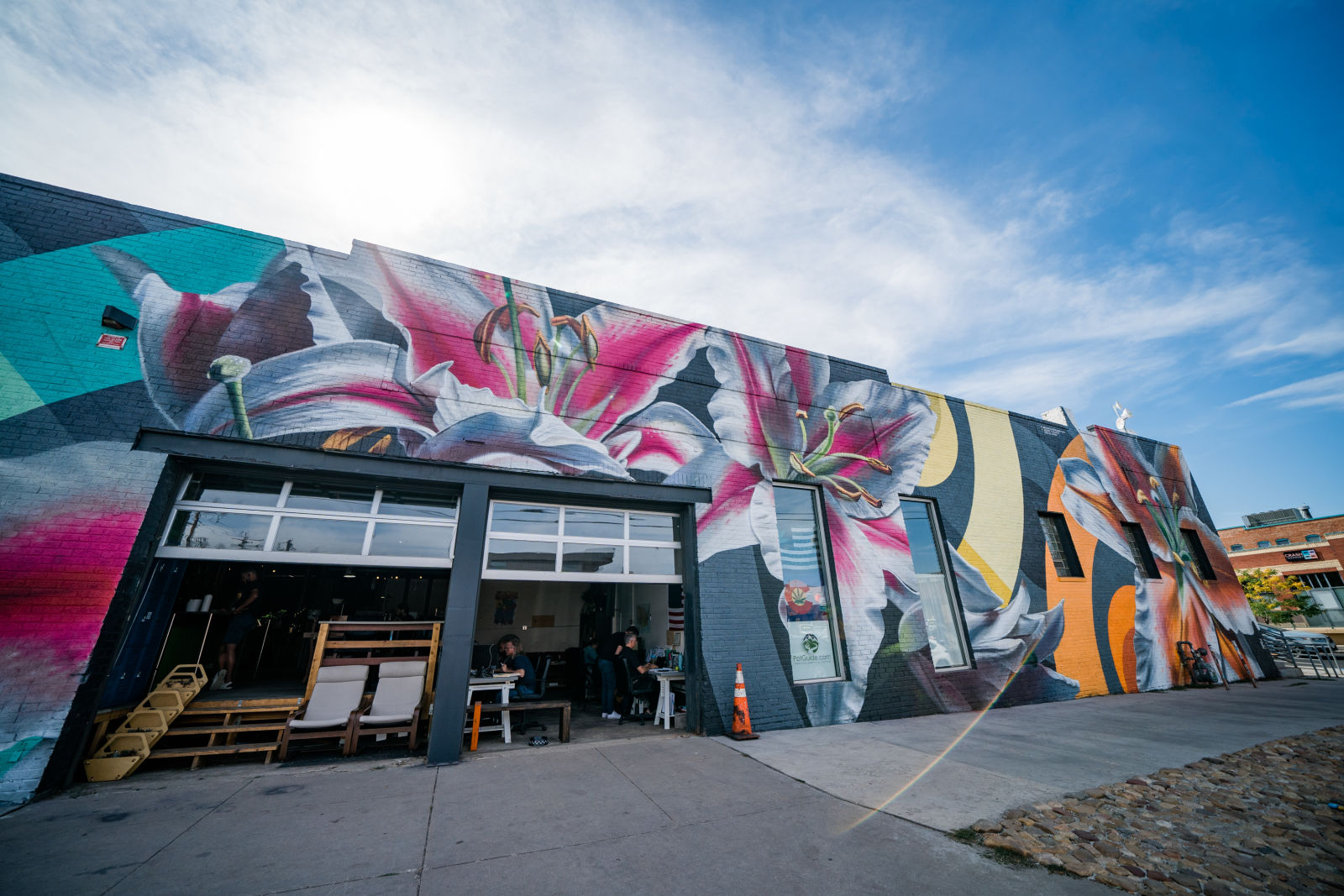 Large pink and white flower murals across a building with garage doors beneath a blue sky